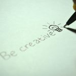 Close-up of handwritten 'Be creative' with a light bulb sketch on paper.