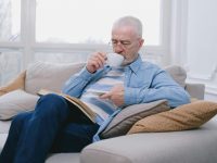 pexels-photo-7545180-7545180 Elderly man enjoying a peaceful moment on sofa with a hot drink and book.